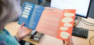Een vrouw houdt een brochure voor een computer en bespreekt "Seksuele grensoverschrijding in het mbo". School en Veiligheid
