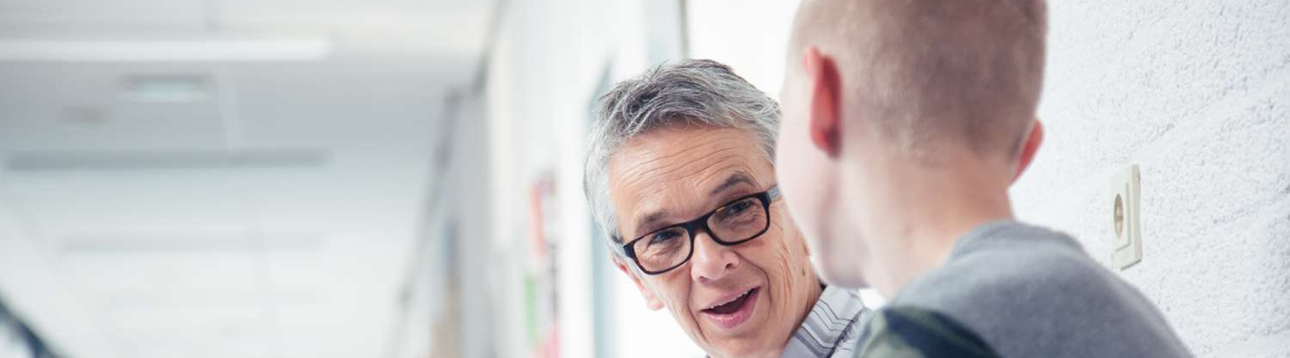 In een gang voeren een man met een bril en een andere man een boeiend gesprek. School en Veiligheid