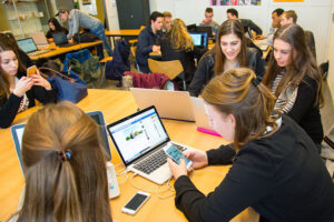 Een groep mensen in de mbo-setting die met laptops rond een tafel zitten en verwikkeld zijn in "Pesten in het mbo"-gesprekken. School en Veiligheid