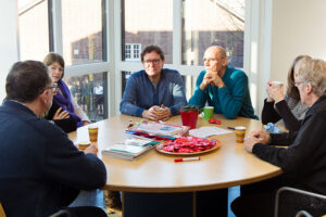 Een groep mensen die rond een tafel zitten en meedoen aan Pesten in het mbo. School en Veiligheid