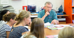 Een groep mensen die in een klaslokaal rond een tafel zitten en zich bezighouden met pesten in het voortgezette onderwijs. School en Veiligheid