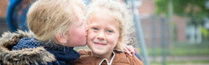 Twee kleine meisjes kussen elkaar liefdevol op de wang en tonen onschuldige uitingen van vriendschap en kameraadschap. School en Veiligheid