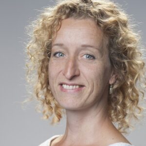 Emily, een vrouw met krullend haar, glimlachend naar de camera. School en Veiligheid