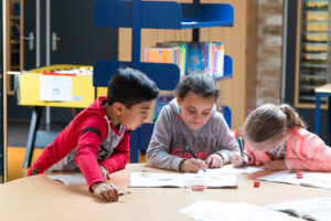 Een groep kinderen bezig met burgerschapsvormingsactiviteiten aan een tafel in een bibliotheek tijdens hun basisonderwijs. School en Veiligheid