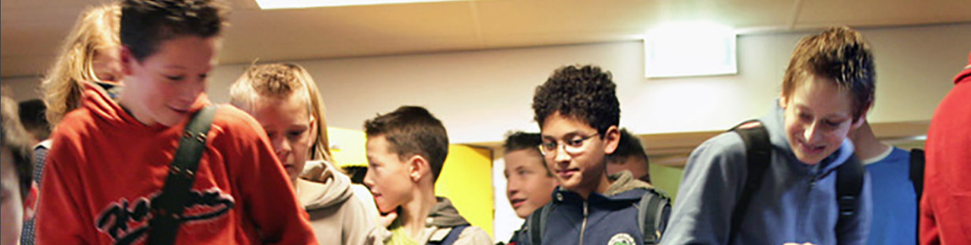 Een groep mensen staat in een gang en bespreekt in een geanimeerd gesprek de Gespreksleidraad 'Samen voor een veilige school'. School en Veiligheid