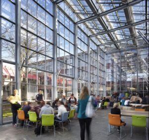 Een groot glazen gebouw waar mensen aan tafels zitten en werken aan het bevorderen van de seksuele integriteit onder studenten. School en Veiligheid