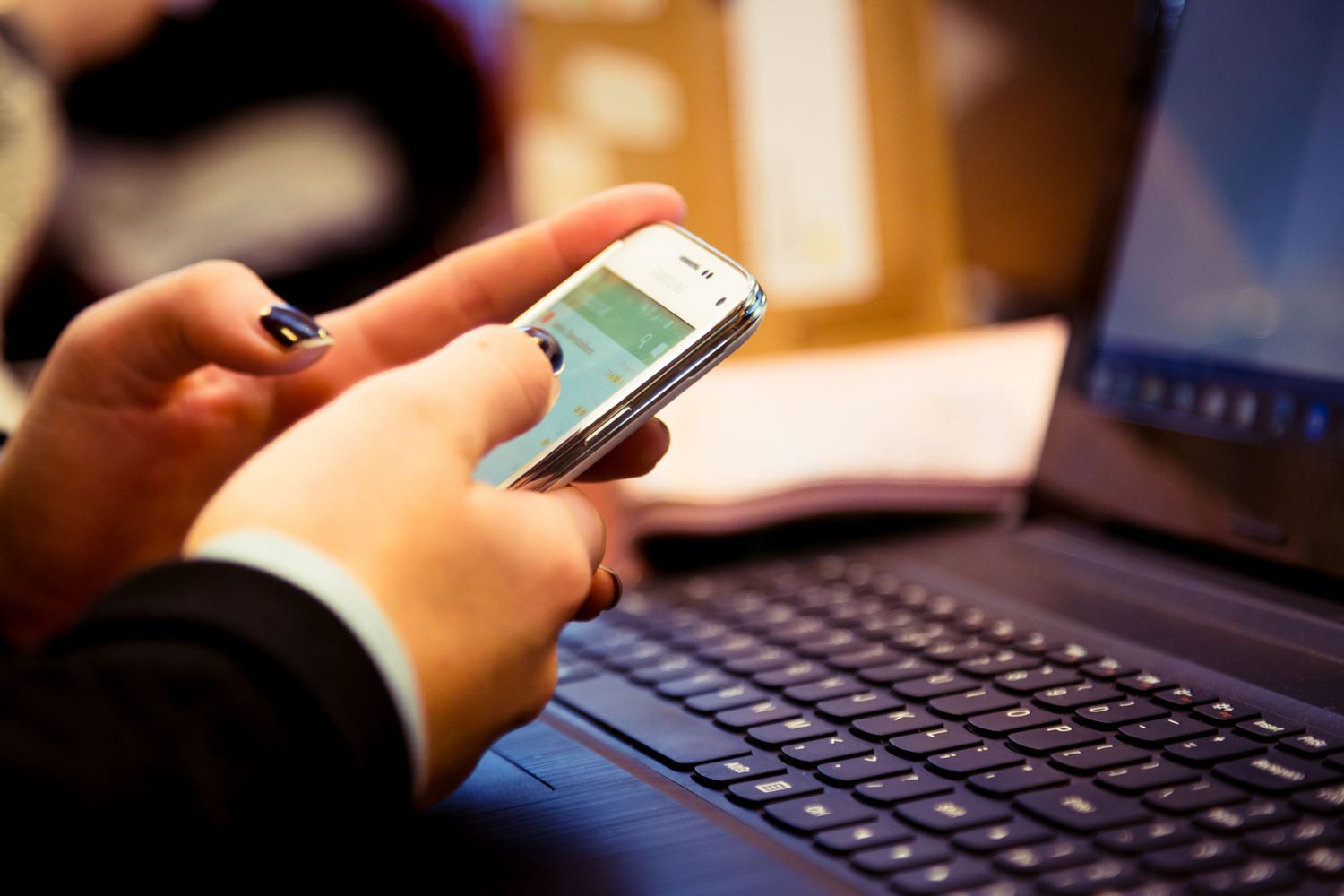 Een persoon die een mobiele telefoon gebruikt terwijl hij op zijn laptop werkt. School en Veiligheid