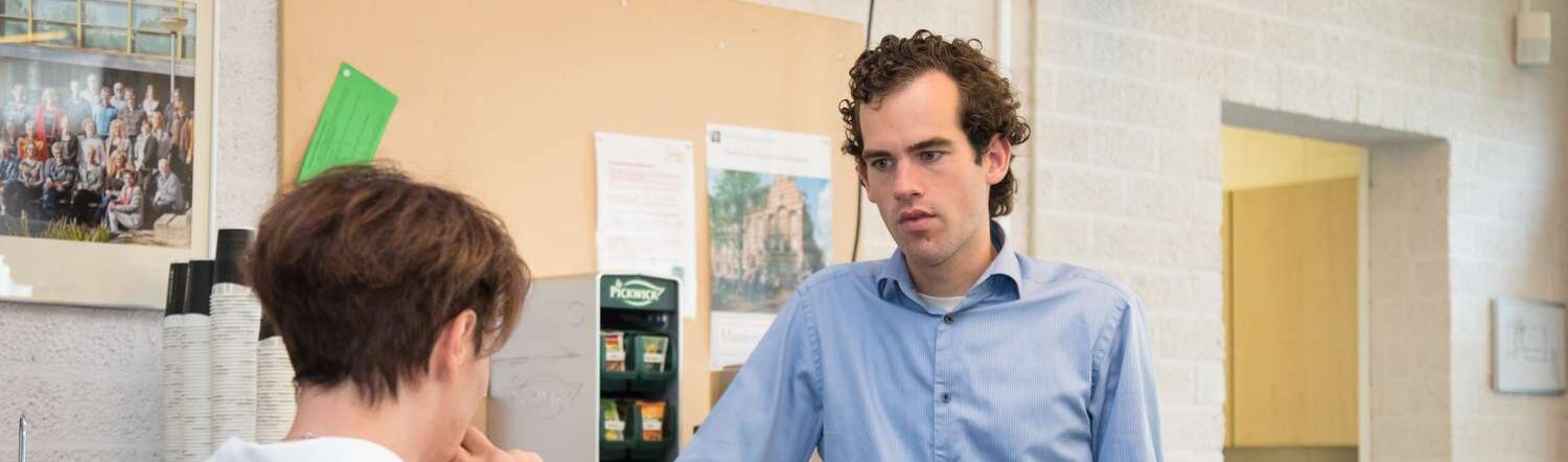 Een man bespreekt klachten met een andere man in een gang. School en Veiligheid