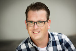 Een man met bril en geruit overhemd geniet van De Gouden en Zilveren Weken. School en Veiligheid