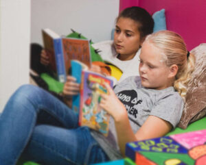 Twee meisjes liggen op bed een boek te lezen en ondersteunen scholen bij het bevorderen van de sociale veiligheid. School en Veiligheid