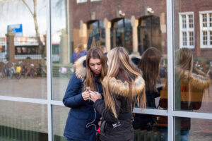 Twee meisjes geobsedeerd door sociale media, verdiept in hun telefoons voor een gebouw. School en Veiligheid