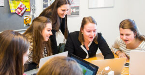 Een groep jonge vrouwen die met laptops rond een tafel zitten en seksuele voorlichting op middelbare scholen bespreken en onderzoeken. School en Veiligheid