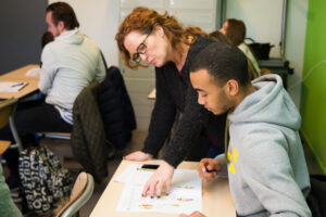Een vrouw die in een klaslokaal begeleiding geeft op het gebied van seksualiteit aan een mbo-student. School en Veiligheid