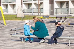 Een vrouw en twee kinderen bezig met vertrouwenswerk terwijl ze op een bankje in het primair onderwijs zitten. School en Veiligheid