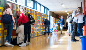 Een groep mensen in een gang met kleurrijke kluisjes, actief bezig met discussies over seksuele voorlichting op middelbare scholen. School en Veiligheid