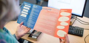 Een vrouw houdt een brochure voor een computer en bespreekt "Seksuele grensoverschrijding in het mbo". School en Veiligheid