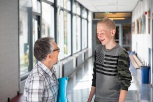 Een jonge jongen is bezig met vertrouwenswerk terwijl hij met een oudere man praat in een gang op het voortgezet onderwijs. School en Veiligheid