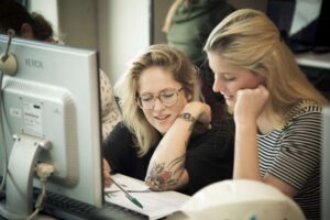 Twee vrouwen werken op een computer op een kantoor en bespreken kwesties van seksuele grensoverschrijding in het voortgezet onderwijs. School en Veiligheid