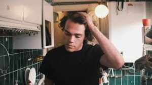 Een man in een zwart shirt die in een keuken staat en het project Genderwijs en de bijdrage ervan aan gendergelijkheid in het onderwijs onder de aandacht brengt. School en Veiligheid