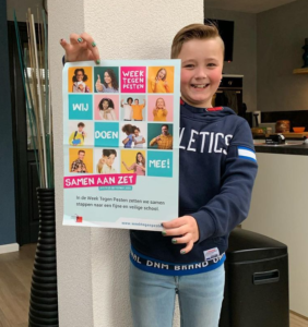 Een jonge jongen houdt een poster omhoog, waarmee hij scholen ondersteunt bij het bevorderen van de sociale veiligheid. School en Veiligheid