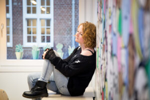 Een vrouw zittend op een bankje voor een muur vol graffiti, nadenkend over Stil Verdriet. School en Veiligheid