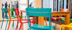 Een rij kleurrijke stoelen naast een houten tafel ter bevordering van gender- en seksuele diversiteit in het mbo. School en Veiligheid