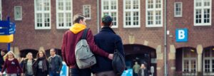 Twee individuen met verschillende geslachtsidentiteiten die met rugzakken over straat lopen. School en Veiligheid