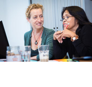 Twee vrouwen zitten aan een tafel en ondersteunen scholen bij het bevorderen van de sociale veiligheid terwijl ze naar een computer kijken. School en Veiligheid