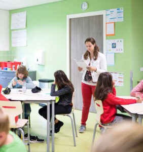 Een leraar in een klaslokaal met kinderen die aan bureaus zitten en scholen ondersteunt met sociale veiligheid. School en Veiligheid