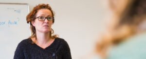 Een vrouw met een bril staat voor een whiteboard en is in gesprek met haar klas over de situatie in Oekraïne. School en Veiligheid