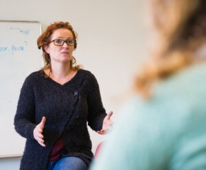 Een vrouw in gesprek met je klas, zittend voor een whiteboard, pratend over de situatie in Oekraïne. School en Veiligheid