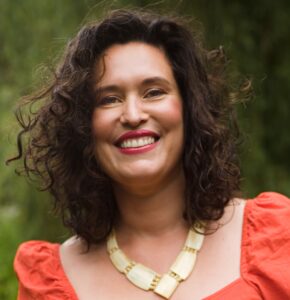 Een lachende vrouw met krullend haar in een oranje topje woont de onderwijsconferentie bij. School en Veiligheid