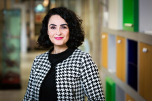 Een vrouw in een zwart-wit pied-de-poule jasje in een gang tijdens de Onderwijsconferentie. School en Veiligheid