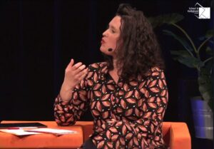 Een vrouw zit in een oranje stoel te praten op een Onderwijsconferentie. School en Veiligheid