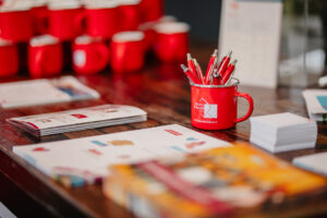 Rode mok gevuld met pennen op tafel, omringd door brochures en promotiemateriaal, op de Onderwijsconferentie Met Alle Respect! evenement. School en Veiligheid