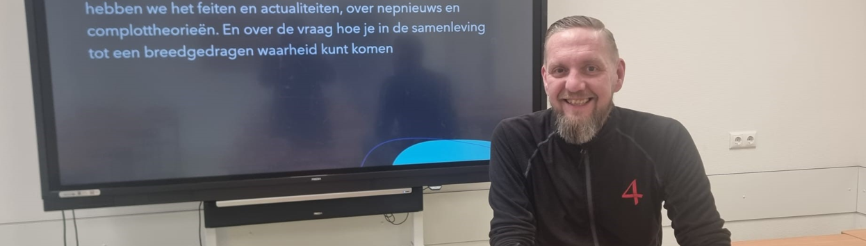 Glimlachende man zittend aan een tafel voor een televisie met tekst over spanning en discussie in de klas. School en Veiligheid